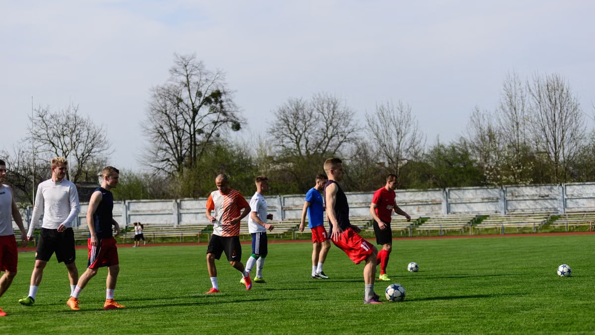 Athletes practicing soccer outdoors on a lush green field under clear skies.